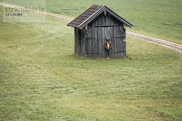 Junger Mann vor einer Holzhütte auf einer Wiese stehend