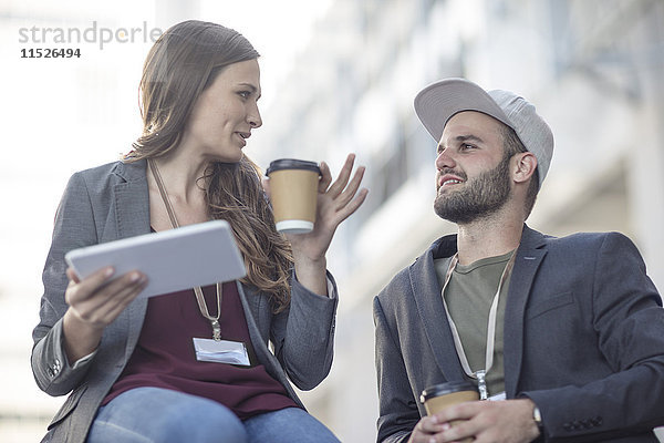 Junger Mann und Frau mit Tablette und Kaffee zum Reden im Freien