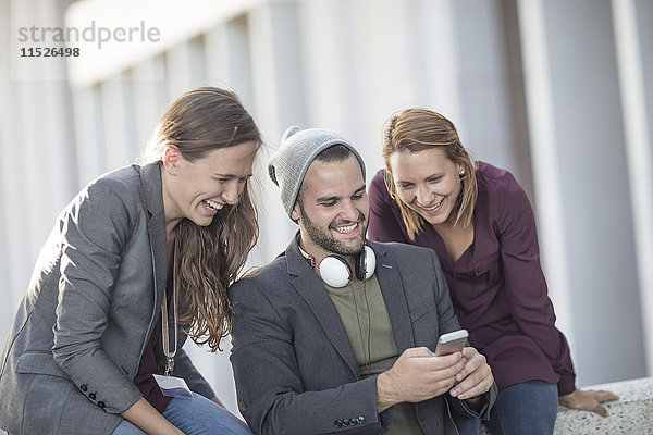 Drei fröhliche junge Leute schauen gemeinsam aufs Handy