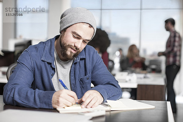 Mann beim Schreiben von Notizen am Schreibtisch im Büro