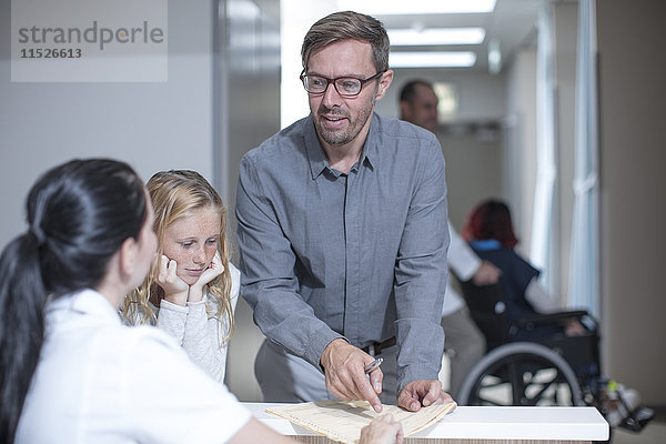 Vater und Tochter stehen an der Rezeption im Krankenhaus