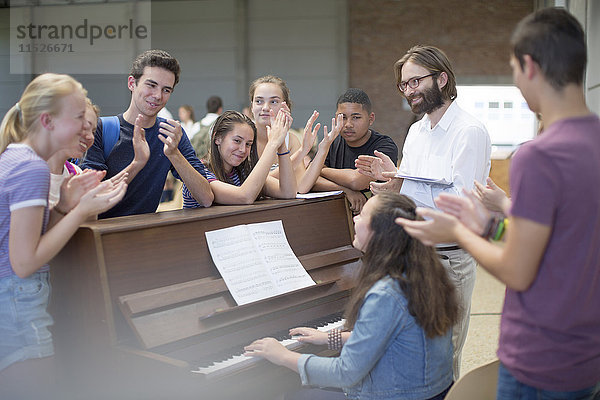 Lehrer mit einer Gruppe von Schülern  die um das Klavier herum stehen und applaudieren.