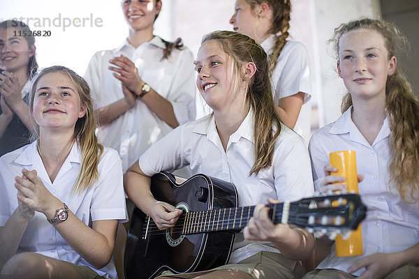 Gymnasiastin beim Gitarrespielen mit einer Gruppe von Schulfreunden im Freien