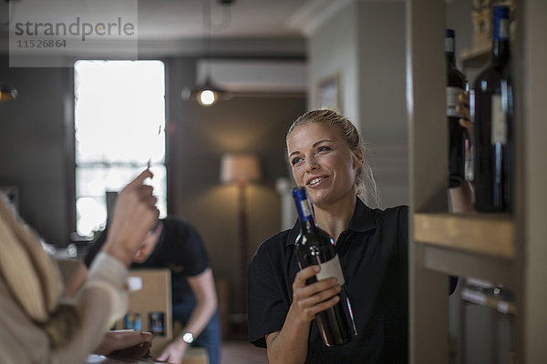 Lächelnde Verkäuferin beim Verpacken von Weinflaschen im Regal in der Weinhandlung
