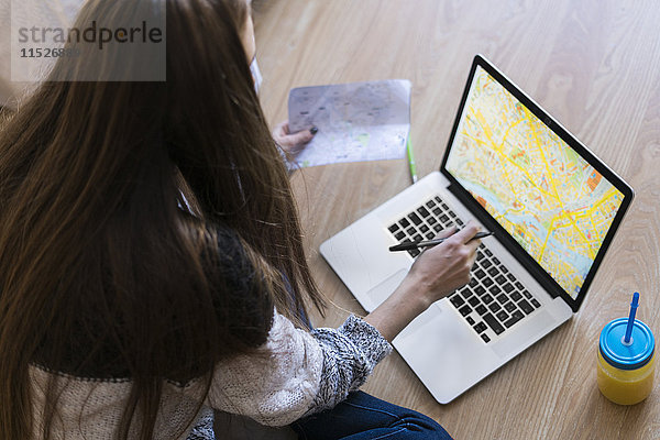Junge Frau auf dem Boden sitzend mit Blick auf die Karte auf dem Laptop