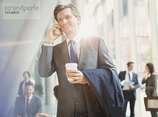 Lächelnder Geschäftsmann mit Kaffee am Handy in der Bürolobby