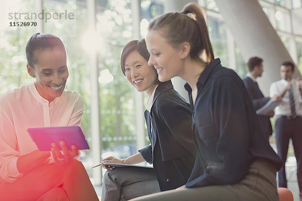 Lächelnde Geschäftsfrauen mit digitalem Tablett  Besprechung in der Bürolobby