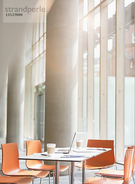 Laptop  Kaffee und Papierkram auf dem Tisch im sonnigen Büro