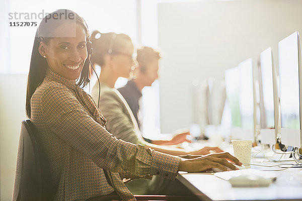 Portrait lächelnde Telemarketerin mit Headset am Computer im sonnigen Büro