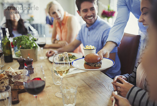 Kellnerin serviert Hamburger an eine Frau  die mit Freunden am Restauranttisch speist.