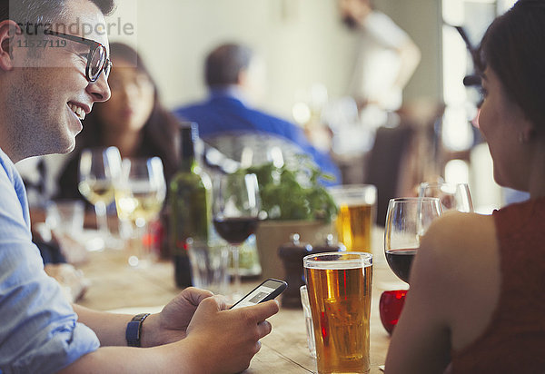 Paar mit Handy sprechen und Bier und Wein am Restauranttisch trinken