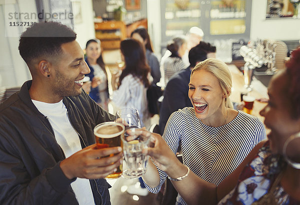 Lachende Freunde toasten Bier und Weingläser an der Bar