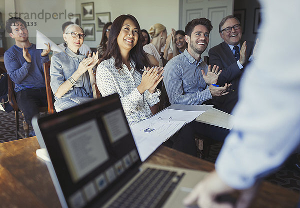 Lächelnde Geschäftsleute klatschen für den Geschäftsmann  der die Konferenz am Laptop leitet.