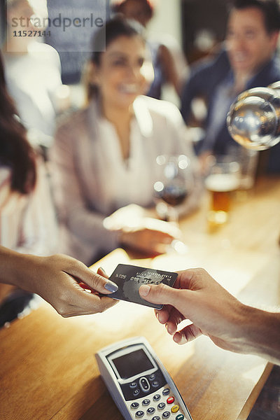 Frau bezahlt Barkeeperin mit Kreditkarte an der Bar