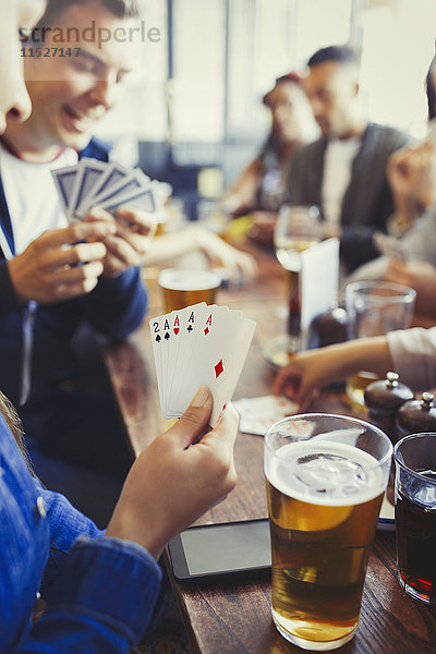 Frau hält Asse in der Hand  spielt Poker und trinkt Bier mit Freunden an der Bar.