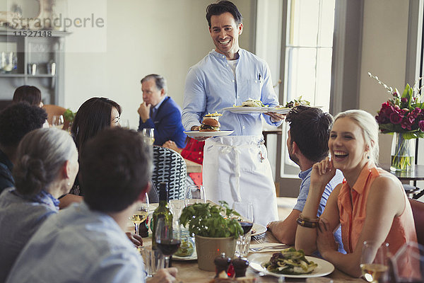 Lächelnder Kellner serviert Essen für Freunde  die am Restauranttisch speisen.