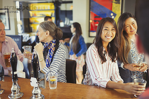 Frauen lächeln dem Barkeeper zu und trinken an der Bar.
