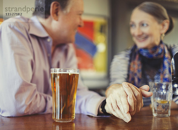 Seniorenpaar hält Händchen und trinkt Bier an der Bar.
