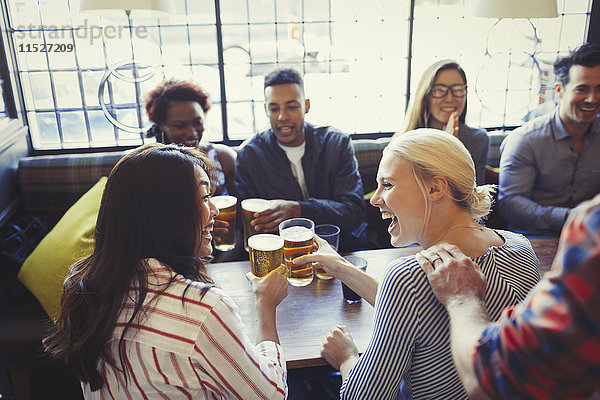 Lachende Freunde toasten Biergläser am Tisch in der Bar