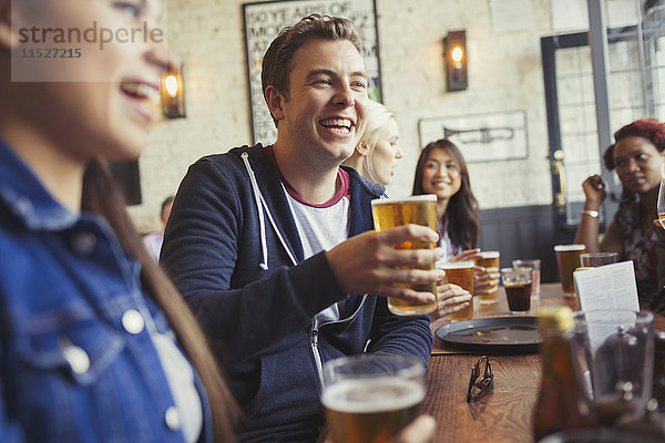 Lächelnder Mann beim Biertrinken mit Freunden am Tisch in der Bar