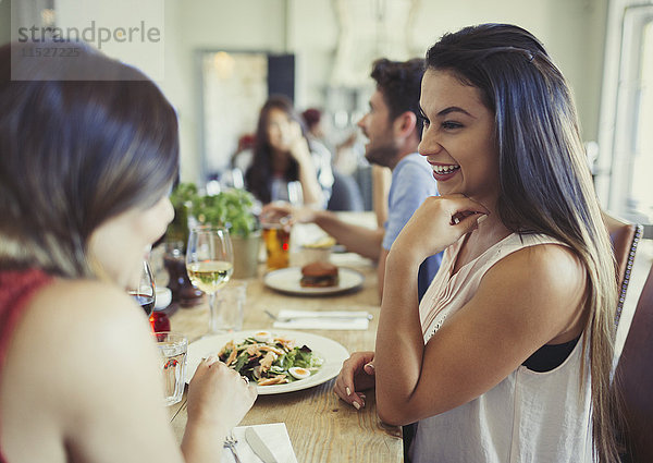 Lächelnde Freundinnen beim Essen und Reden am Restauranttisch