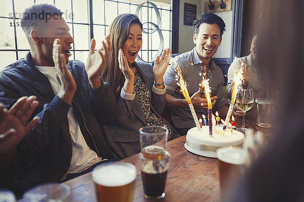 Freunde feiern Geburtstag mit Feuerwerkstorte am Tisch in der Bar