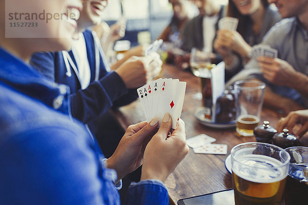 Frau hält Asse  spielt Poker und trinkt Bier mit Freunden am Tisch in der Bar.