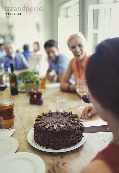 Frau beim Schneiden von Schokoladen-Geburtstagskuchen mit Freunden am Restauranttisch
