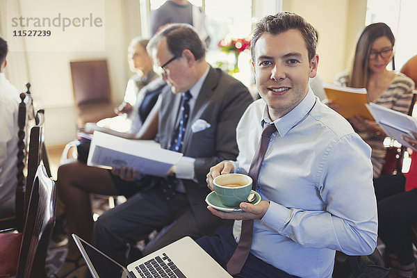 Portrait lächelnder Geschäftsmann  der Kaffee trinkt und den Laptop in der Geschäftskonferenz benutzt.