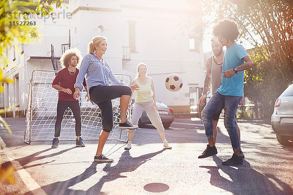 Freunde spielen Fußball in der sonnigen Sommerstraße
