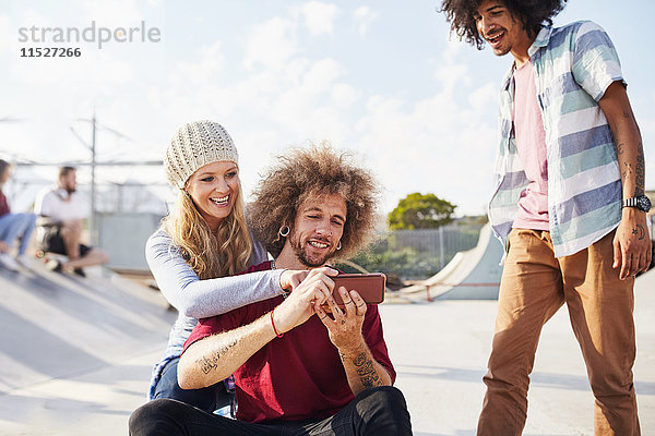 Freunde mit Smartphone im sonnigen Skatepark