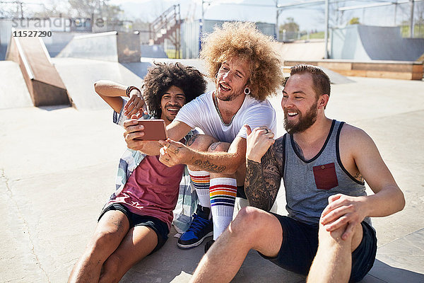 Männliche Freunde mit Fotohandy beim Selfie im sonnigen Skatepark