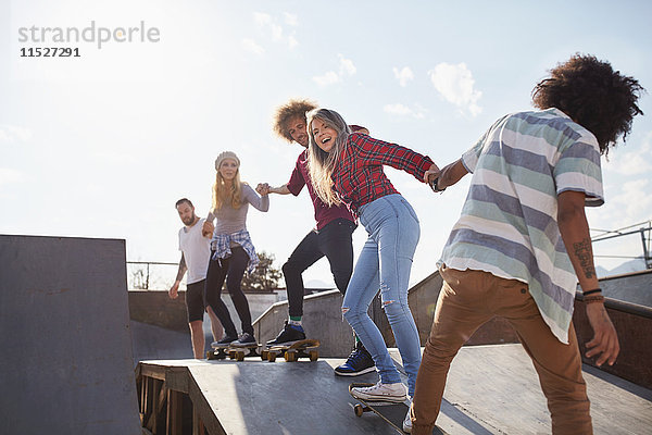 Freunde auf Skateboards halten Hand in Hand auf der Rampe im sonnigen Skatepark.