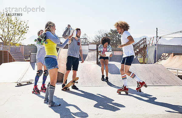 Freunde Rollschuhlaufen und Skateboarden im sonnigen Skatepark