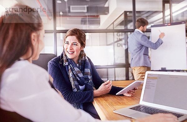 Lächelnde Geschäftsfrauen mit digitalem Tablett und Laptop im Konferenzraumgespräch