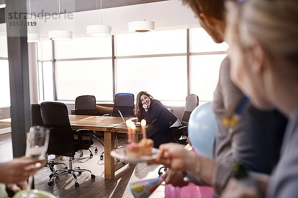 Geschäftsleute überraschen Geschäftsfrau mit Geburtstagskuchen im Konferenzraum