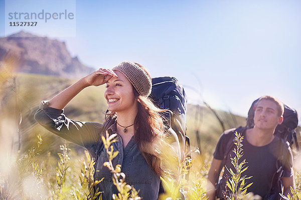 Lächelndes Paar mit Rucksäcken beim Wandern im sonnigen Feld