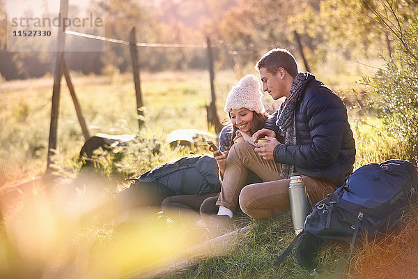 Junge Pärchen  die sich im sonnigen Gras ausruhen  mit Handy und digitalem Tablett