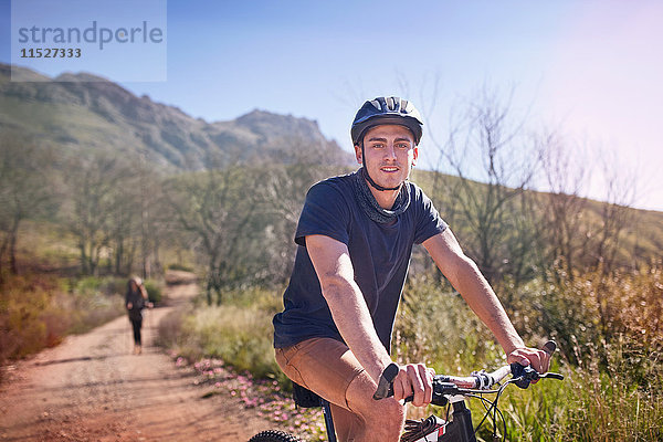 Portrait junger Mann Mountainbiken auf abgelegenem  sonnigem Weg