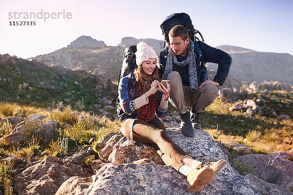 Junges Paar mit Rucksäcken beim Wandern  das sich mit dem Smartphone auf dem Felsen ausruht.