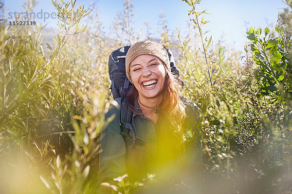Portrait lachende junge Frau mit Rucksackwanderung im sonnigen Feld