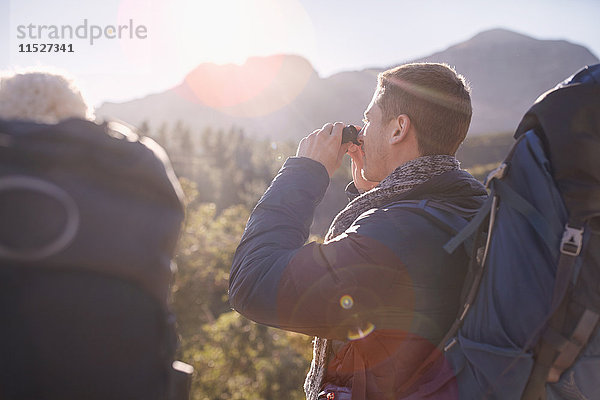 Junger Mann mit Rucksackwanderung mit Fernglas im Sonnenfeld