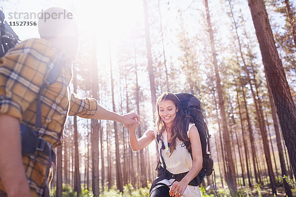 Junger Mann hilft Freundin beim Rucksackwandern im sonnigen Wald