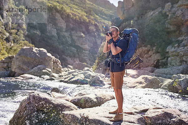 Junger Mann mit Rucksackwanderung  Fotografieren mit Kamera auf sonnigen Felsen