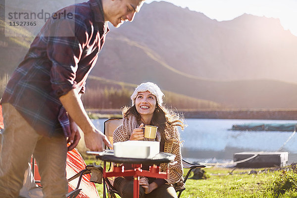 Junges Paar campen  Kochen am Campingkocher am sonnigen Seeufer