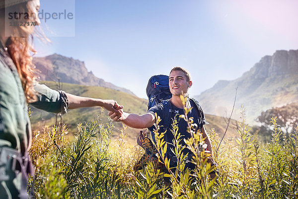 Junges Paar hält Hände beim Wandern im sonnigen Tal