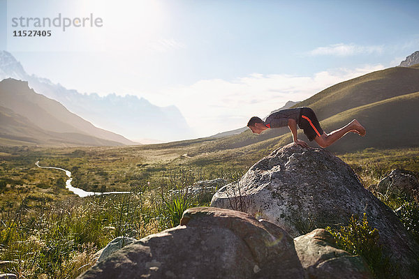 Junger Mann balanciert auf dem Felsen in einem sonnigen  abgelegenen Tal.