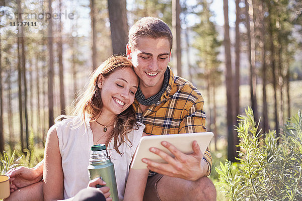 Junges Paar zelten  Kaffee trinken und digitales Tablett in sonnigen Wäldern benutzen