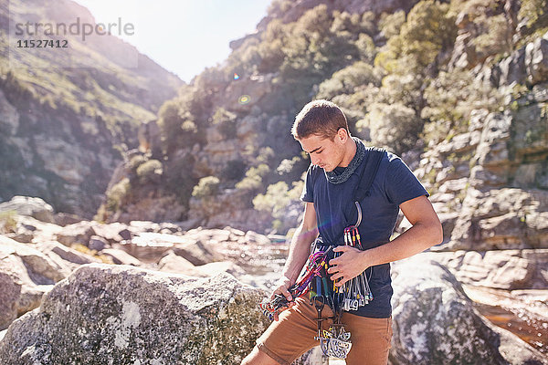 Junger Mann beim Vorbereiten von Kletterkarabinern und Ausrüstung zwischen sonnigen Felsen