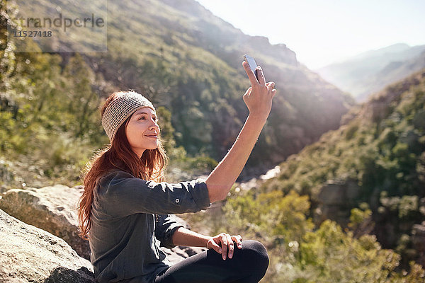 Junge Frau nimmt Selfie mit Fotohandy auf sonnigem  abgelegenem Felsen